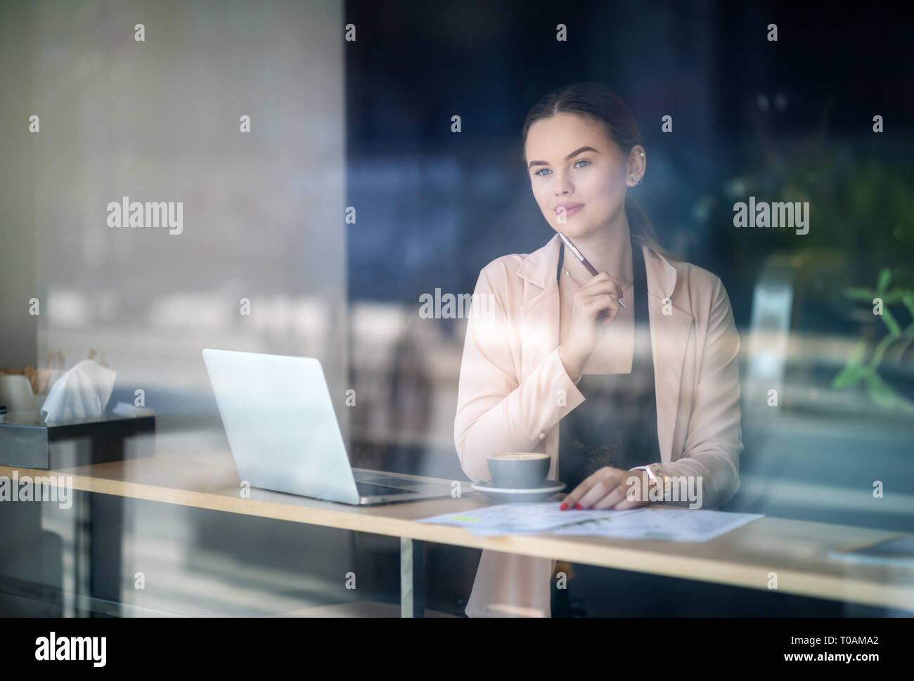 Woman working on laptop at coffee shop. Window Reflexions. Shot of a young woman using a laptop in a cafe Stock Photo