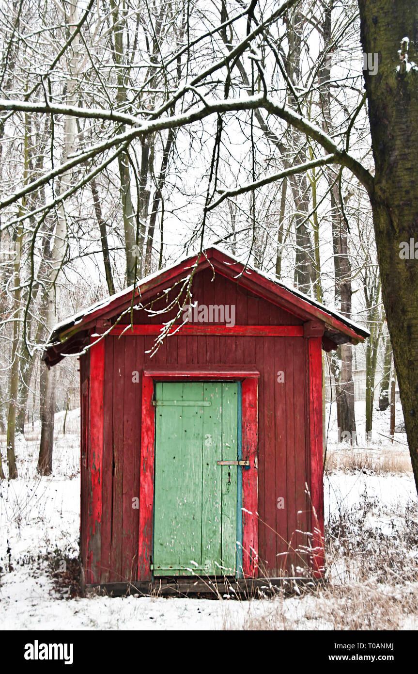red cabin or hut with green door in the forest during snowing in winter Stock Photo