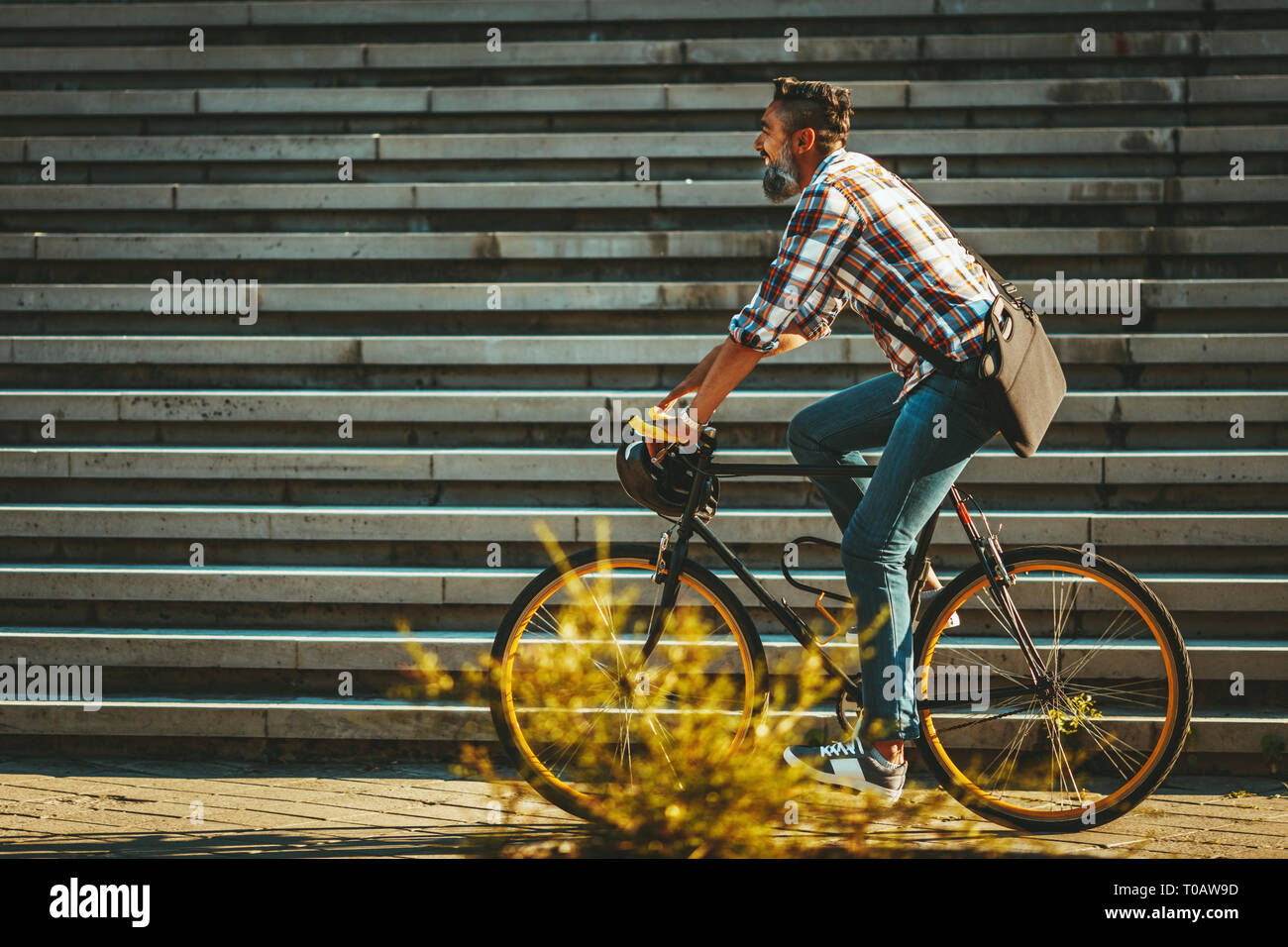 A handsome young man goes to the city with his bike. He is riding the bike, happy because of nice weather. Stock Photo
