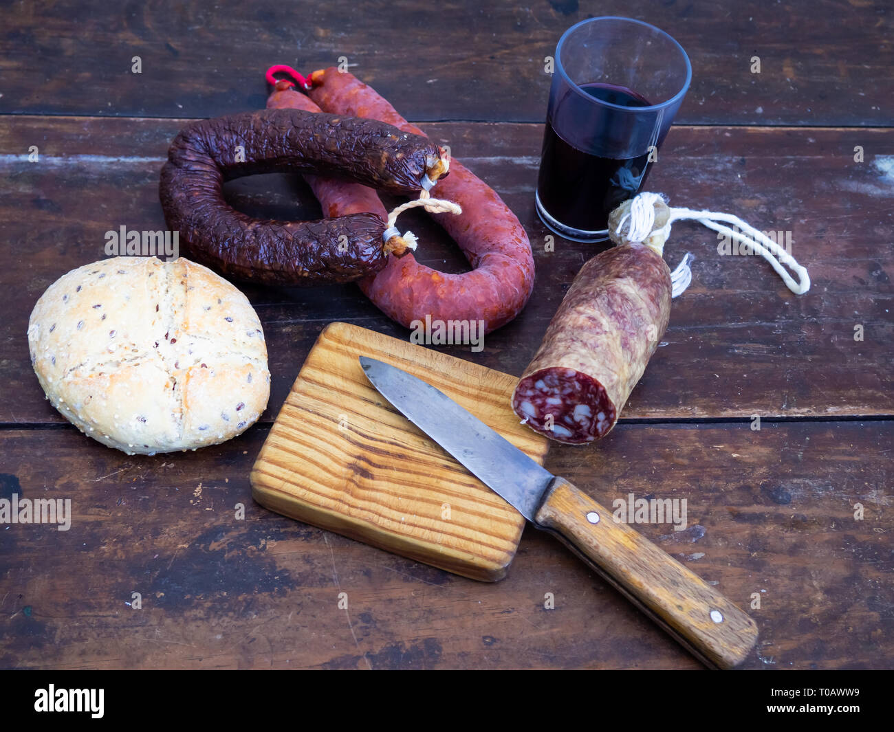 Iberian pork sausages on an old wooden board with a wedge of sheep cheese, an antique knife and a glass of red spanish wine Stock Photo