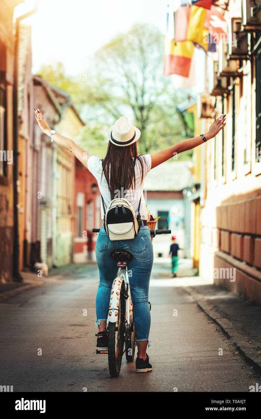 Happy woman is riding the bike along the city street, in summer sunny day, enjoying during outdoor activity. Stock Photo