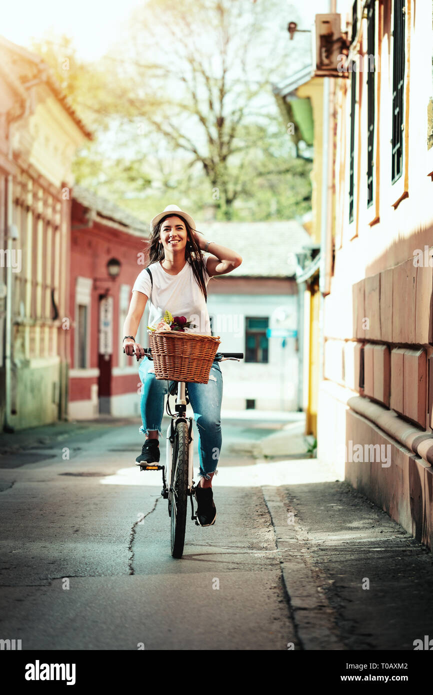 Happy woman riding the bike along the city street, in summer sunny day, smiling of joy during outdoor activity. Stock Photo