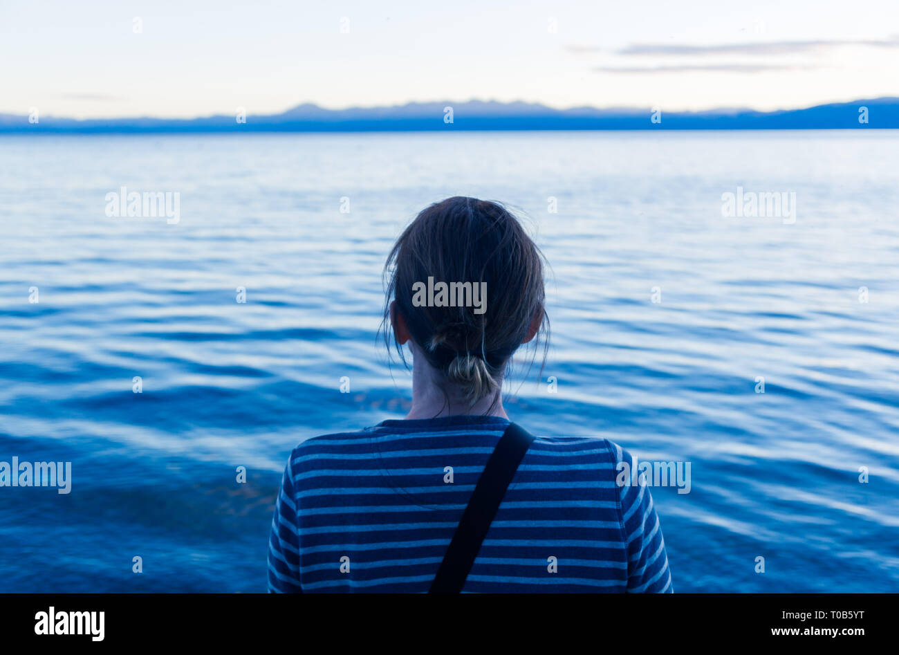 A middle-aged woman sitting and thinking by the water Stock Photo