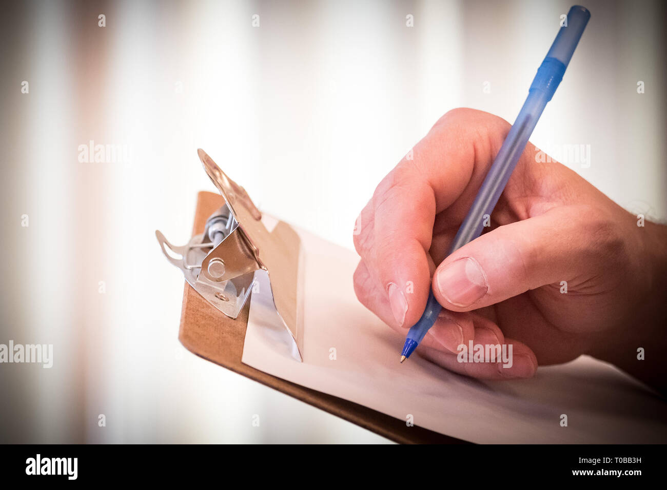 Hand holding blue pen to write checklist, contract, or concept on paper and clipboard Stock Photo
