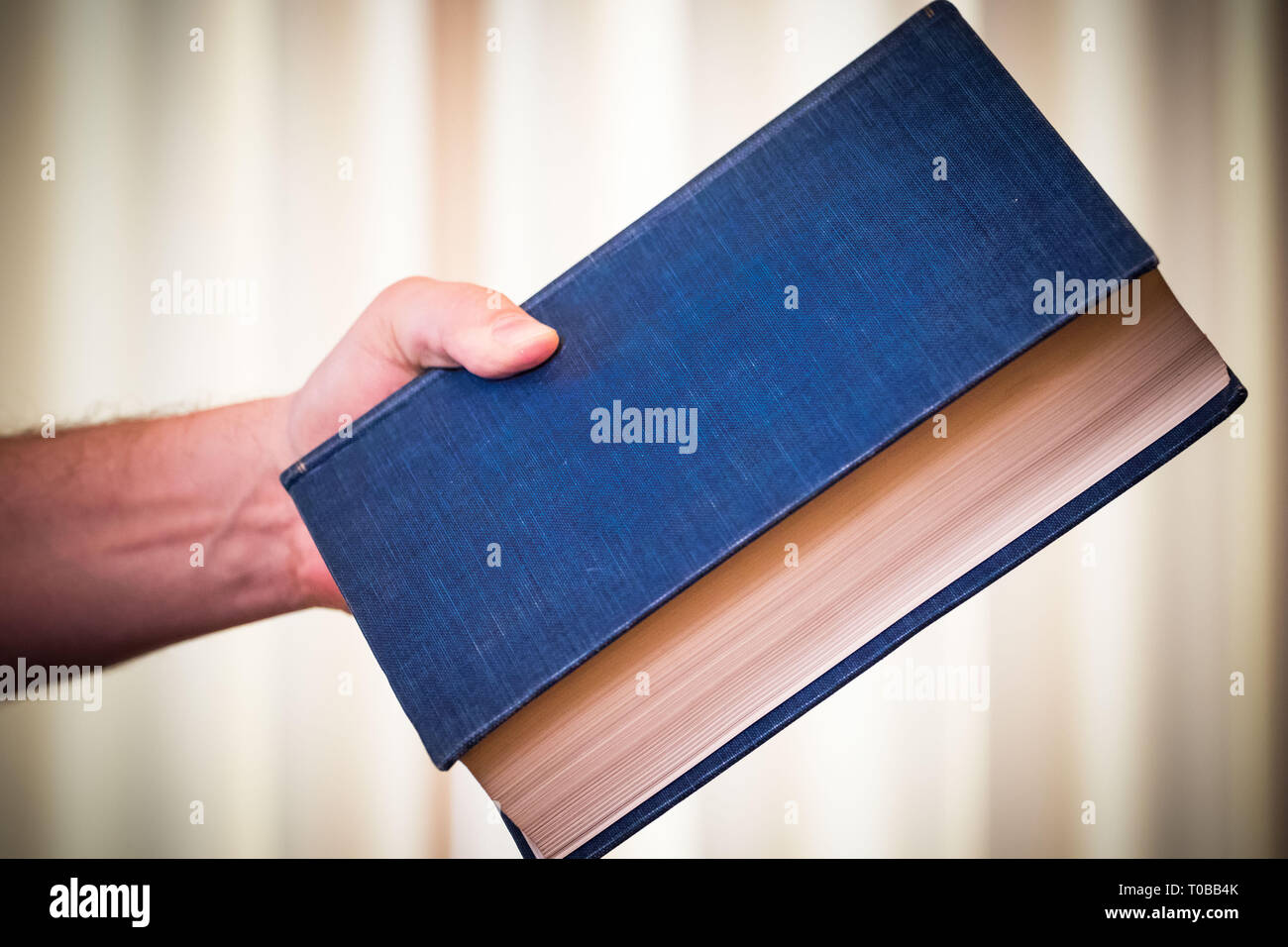 Big heavy blue book in hand; handing to (or throwing the book at) someone. Stock Photo