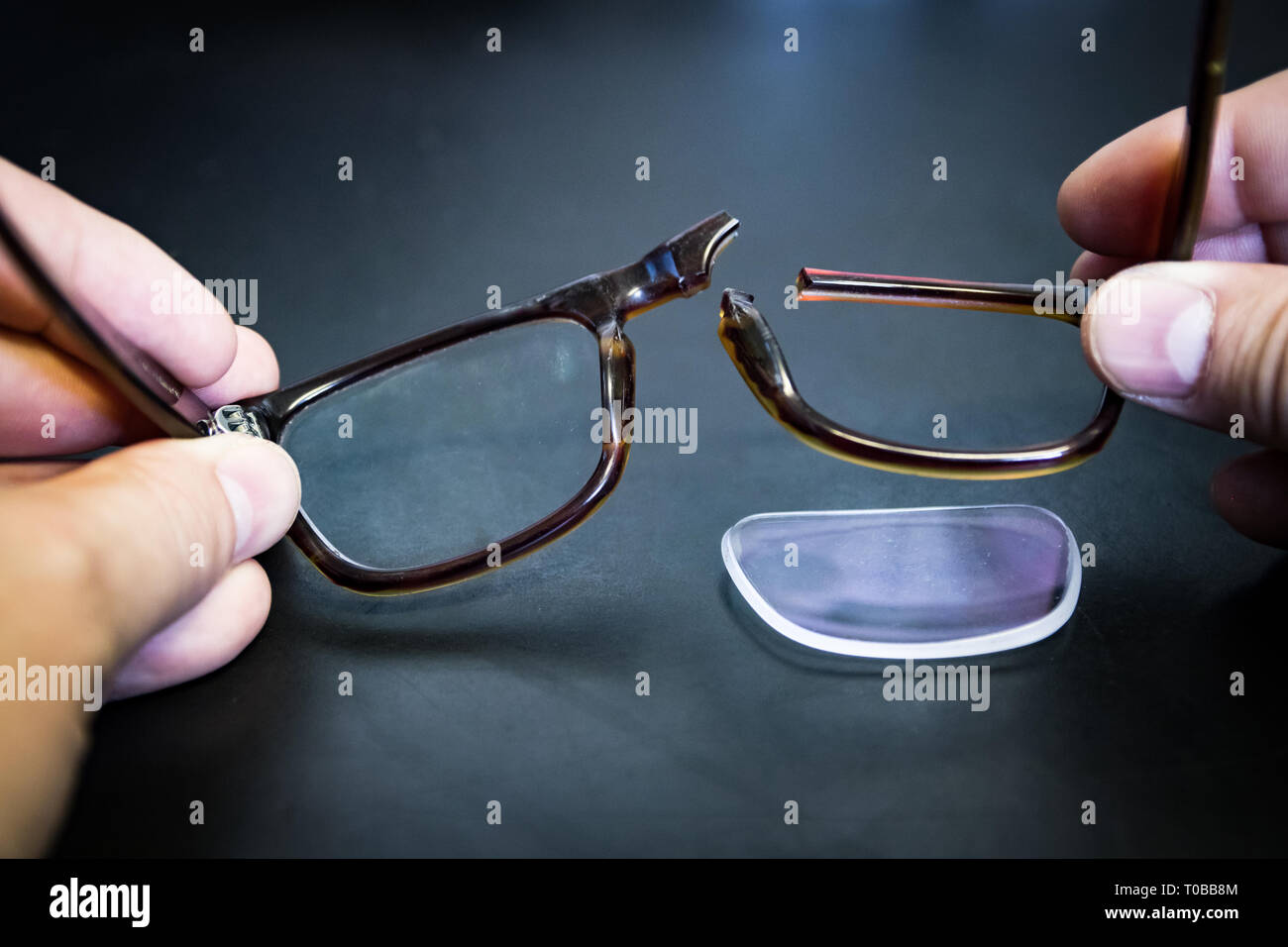 Hands holding broken eyeglasses; lens of glasses fell out of broken
