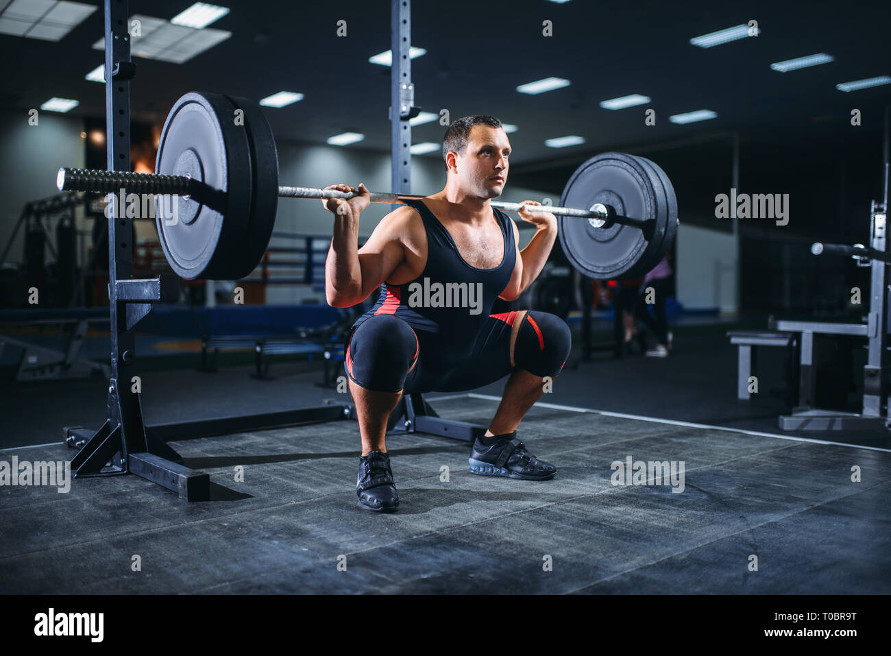 Muscular powerlifter doing squats with barbell in gym. Weightlifting