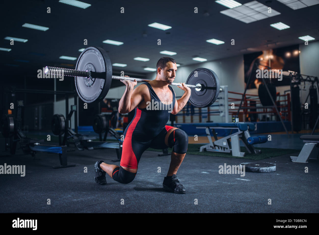 Strong weight lifter doing squats with a barbell in gym deadlift