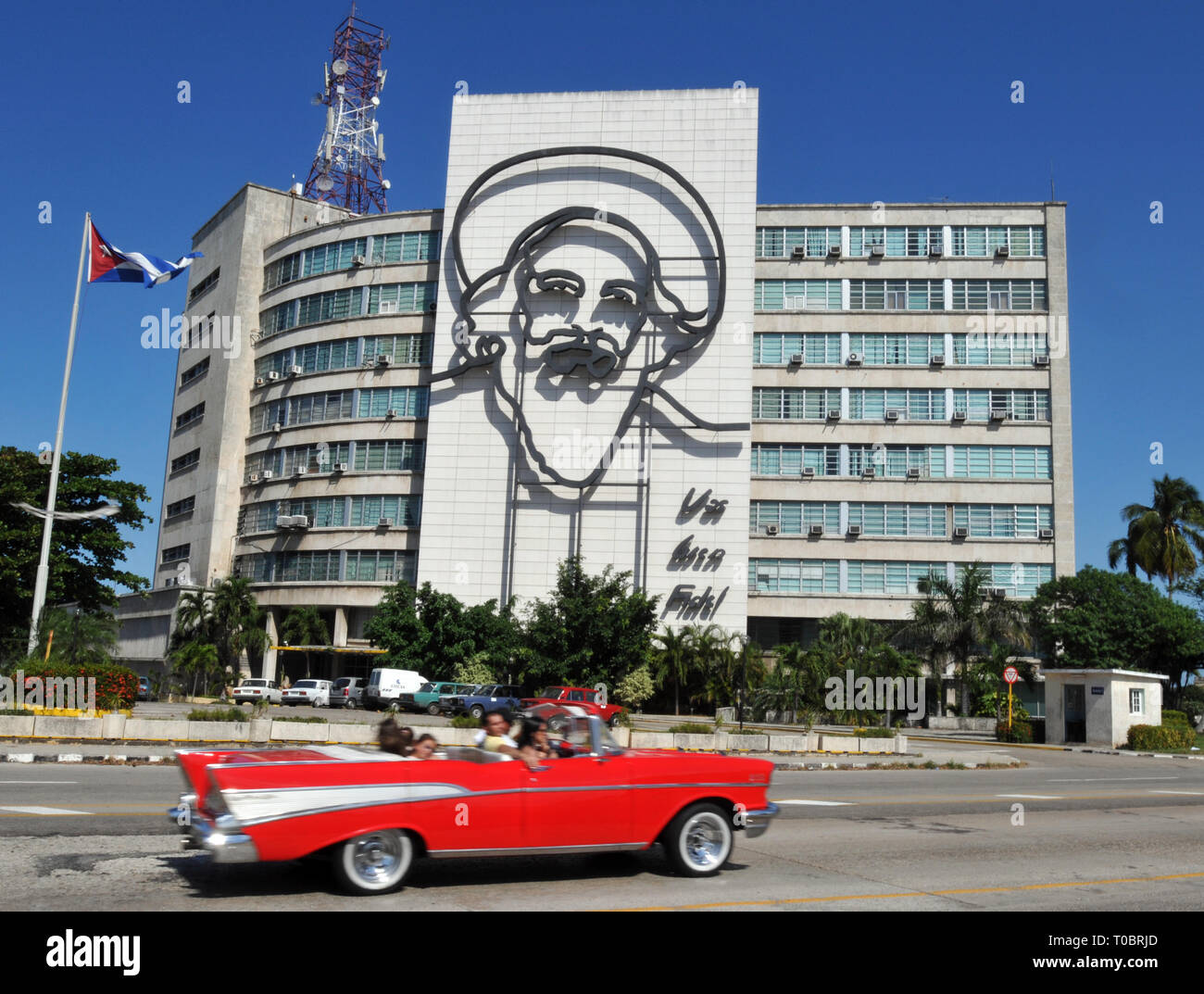 A classic car drives through Havana's Revolution Square, past the Cuban Ministry of Communications building and its sculpture of Camilo Cienfuegos. Stock Photo