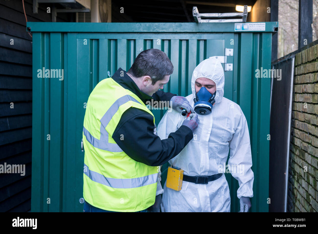 An environmental safety equipped worker in a paper body suit with specialist dust mask has his equipment checked and tested by a coworker / trainer Stock Photo
