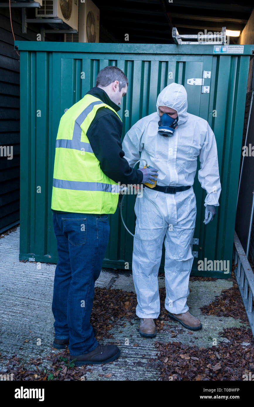 An environmental safety equipped worker in a paper body suit with specialist dust mask has his equipment checked and tested by a coworker / trainer Stock Photo