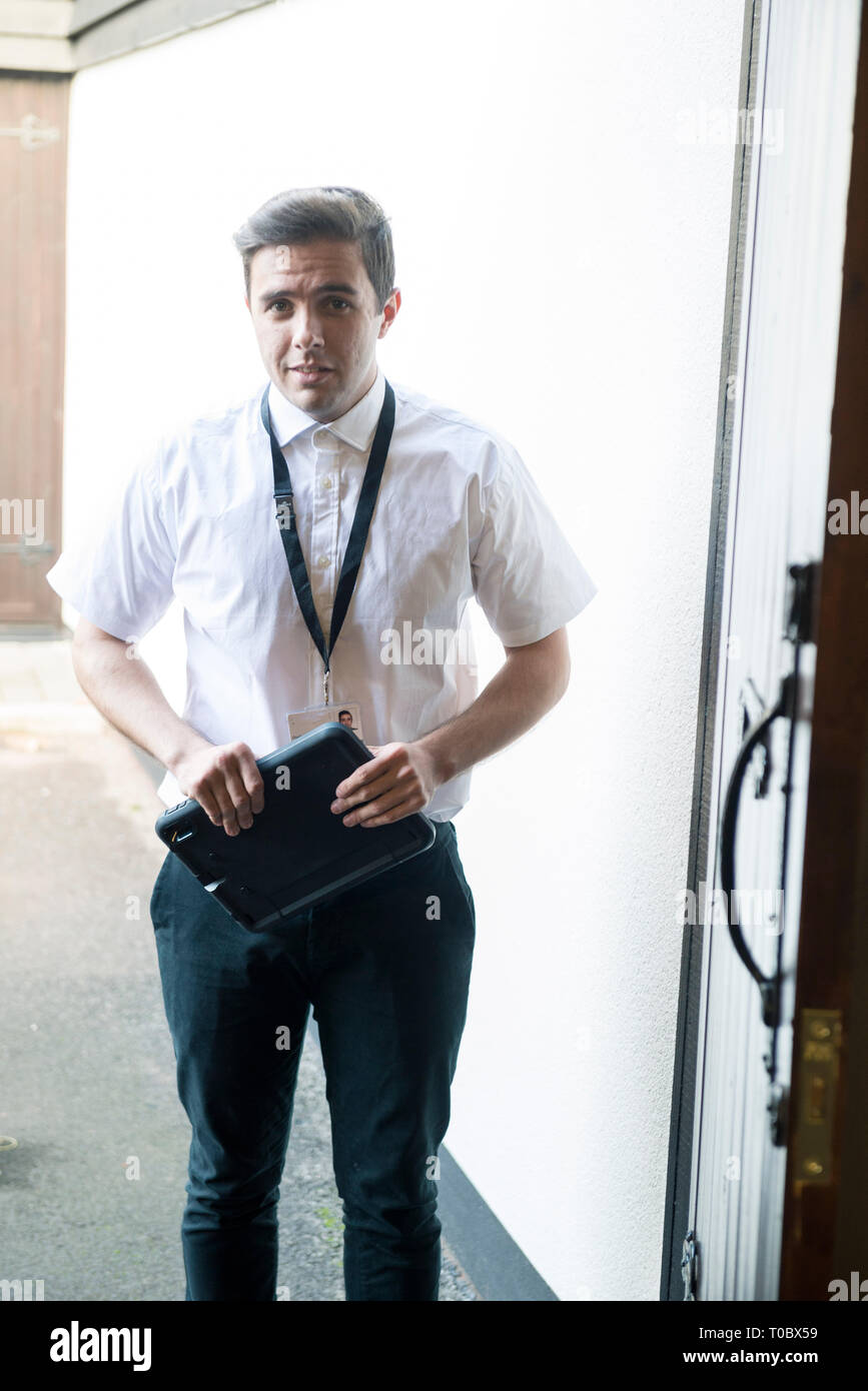 A young white male worker / meter reader / door to door salesman / surveyor, standing in the front door to someone's home after just calling. Stock Photo