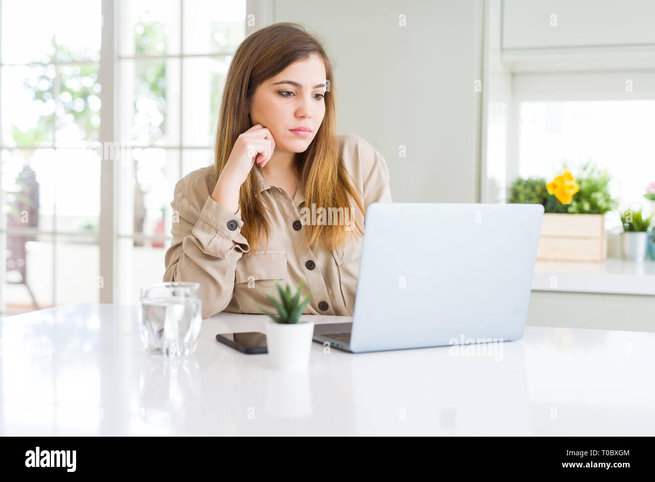 Beautiful young woman using computer laptop serious face thinking about ...
