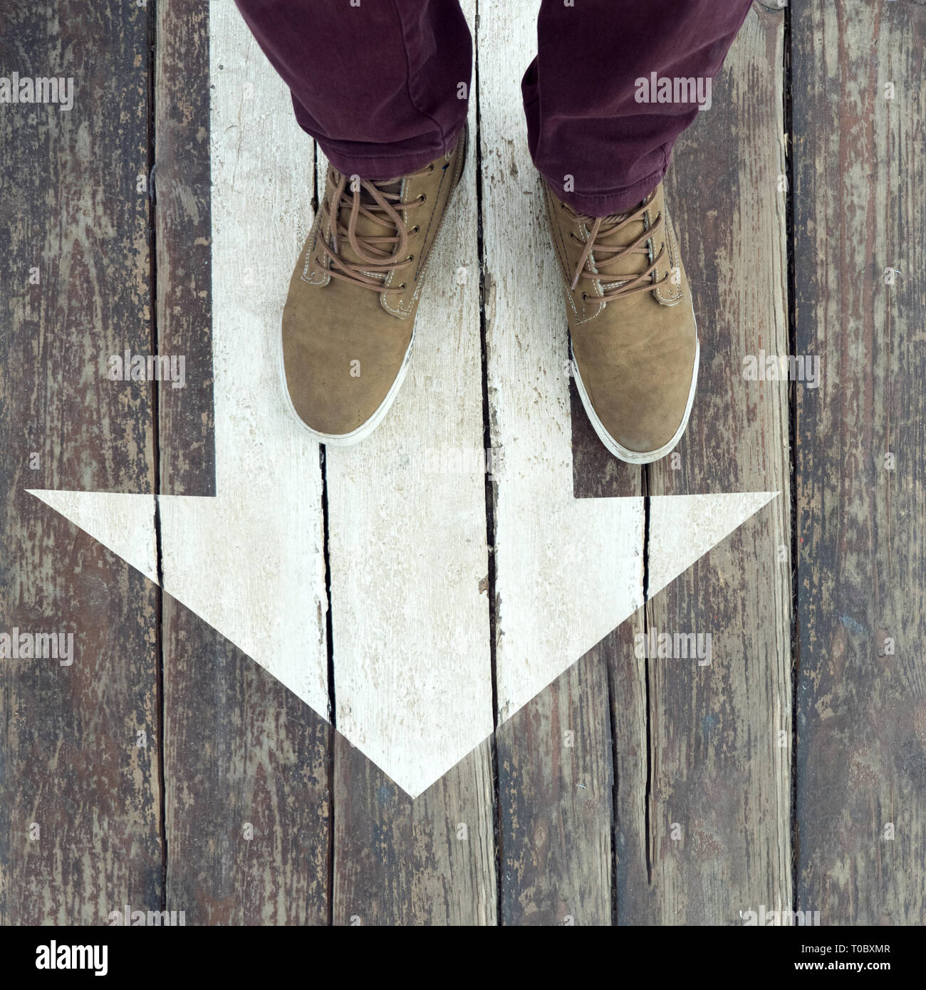 White arrow sign with feet on it. Direction guidline. Following the rules, regulations. Quest background. White sign painted on wooden floor. Guidline Stock Photo