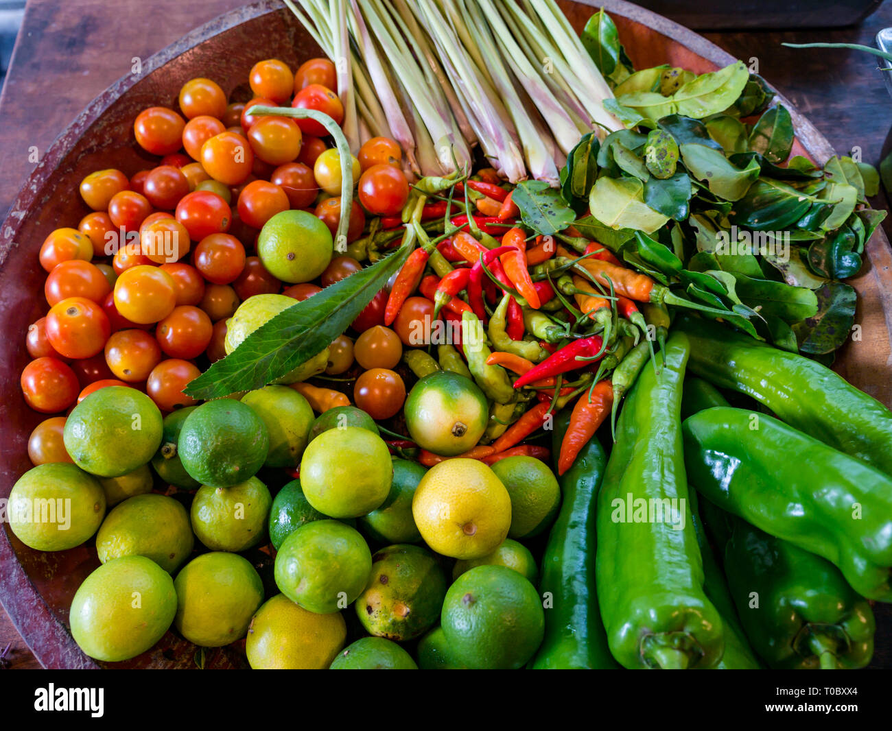 Bowl of colourful fresh ingredients with tomatoes lemongrass limes chillie and peppers at cookery school, Luang Prabang, Laos Stock Photo