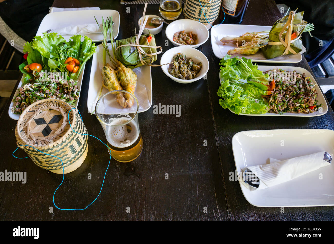 SE Asian Lao dishes on lunch table with rice baskets stuffed lemongrass and sauces at Tamarind cookery school, Luang Prabang, Laos Stock Photo