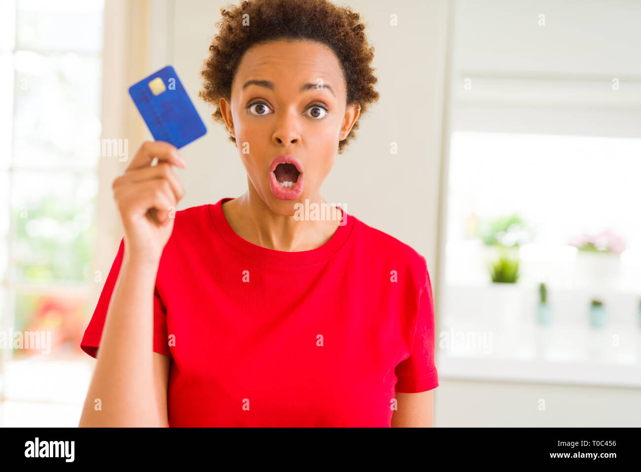Young african american woman holding credit card scared in shock with a ...