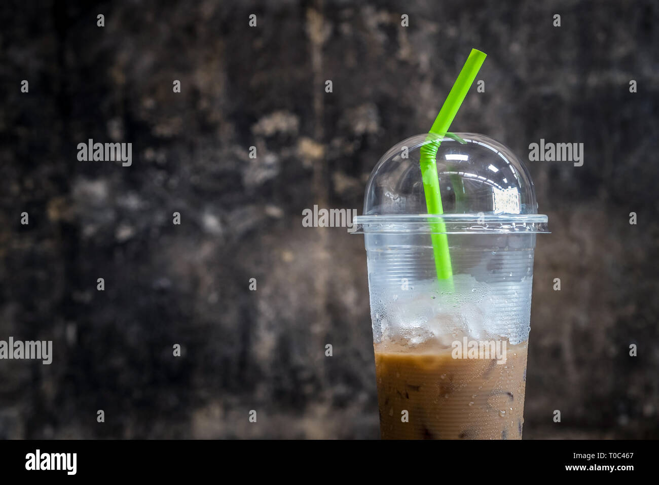 Plastic materials use, show transparent cup and green straw with partly consumed iced coffee inside. Stock Photo