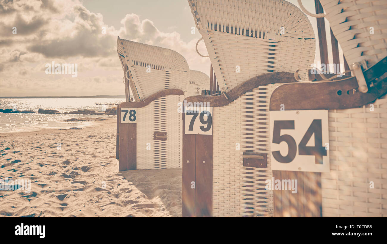 Retro stylized picture of wicker beach chairs on a beach against the sun with lens flare, selective focus. Stock Photo