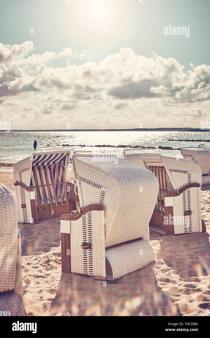 Retro stylized picture of wicker beach chairs on a beach against the sun with lens flare. Stock Photo