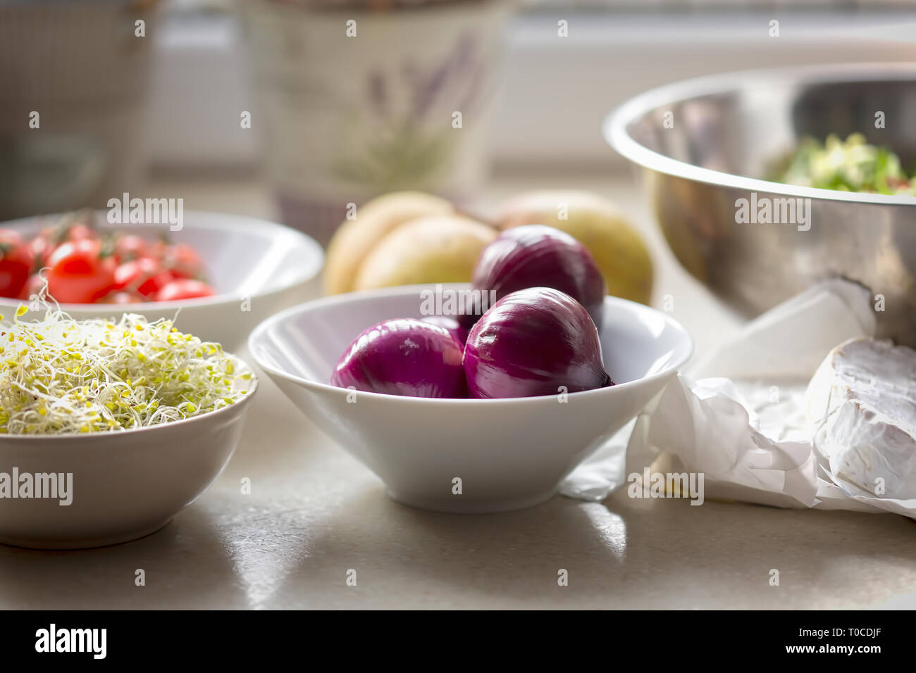 Spring salad ingredients: red onion, tomatoes, mixed leaves lettuce, pears, sprouts, brie on kitchen table Stock Photo