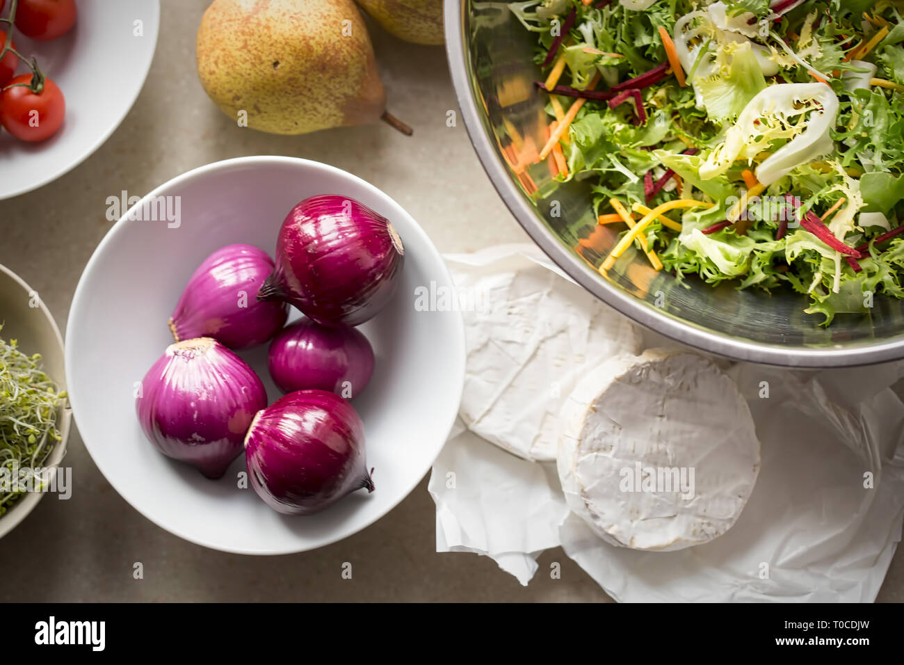 Spring salad ingredients: red onion, tomatoes, mixed leaves lettuce, pears, sprouts, brie on kitchen table Stock Photo