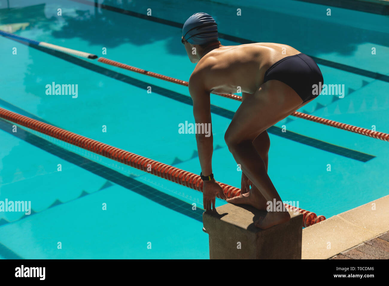 Young male swimmer standing on starting block in starting position at