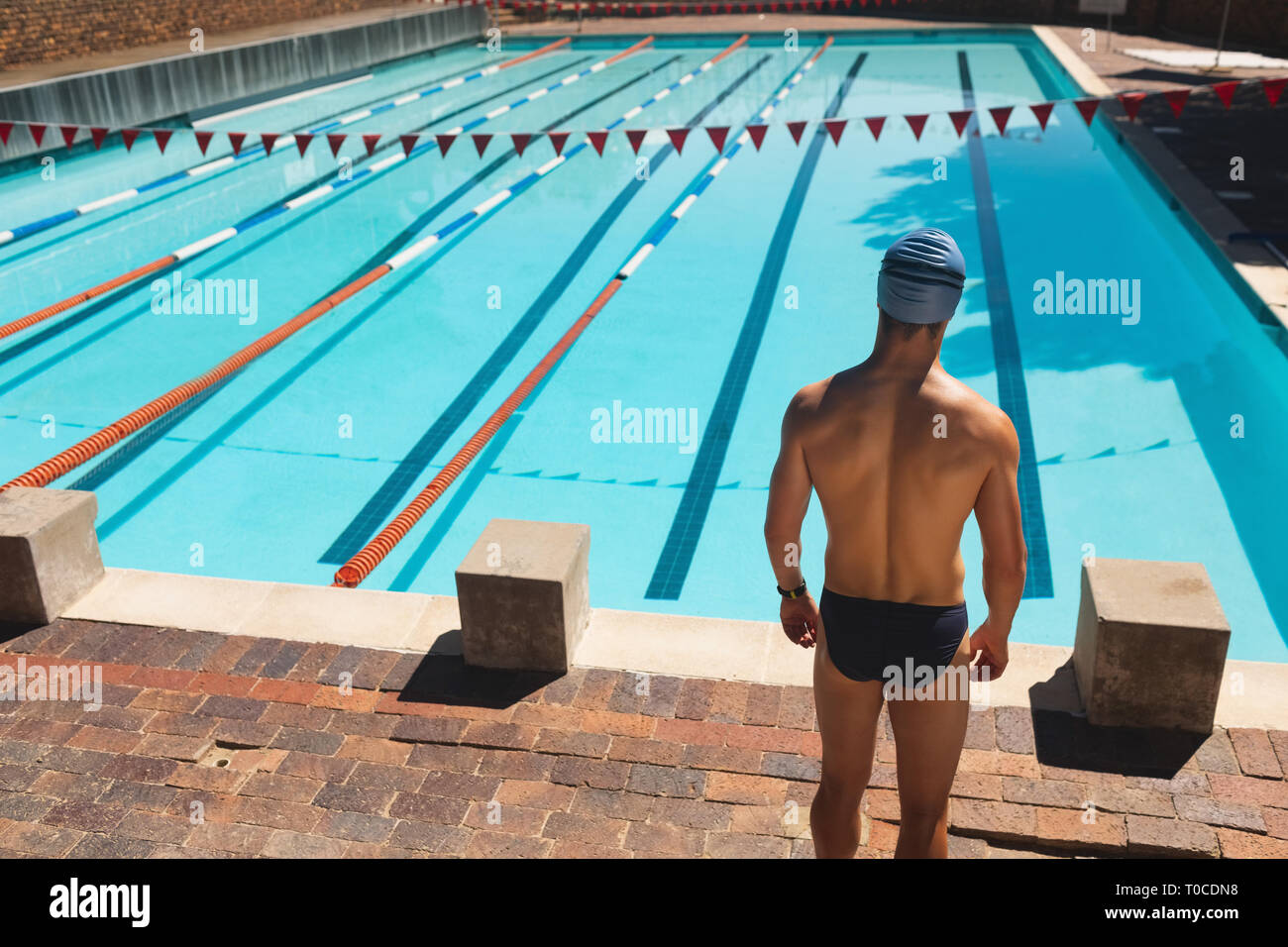Male swimmer standing at the edge of outdoor swimming pool Stock Photo