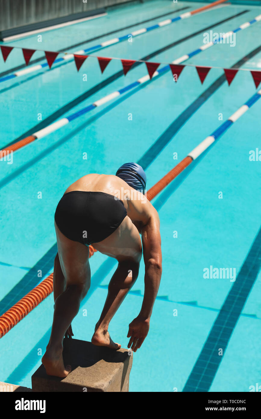 Male swimmer standing on starting block in starting position Stock
