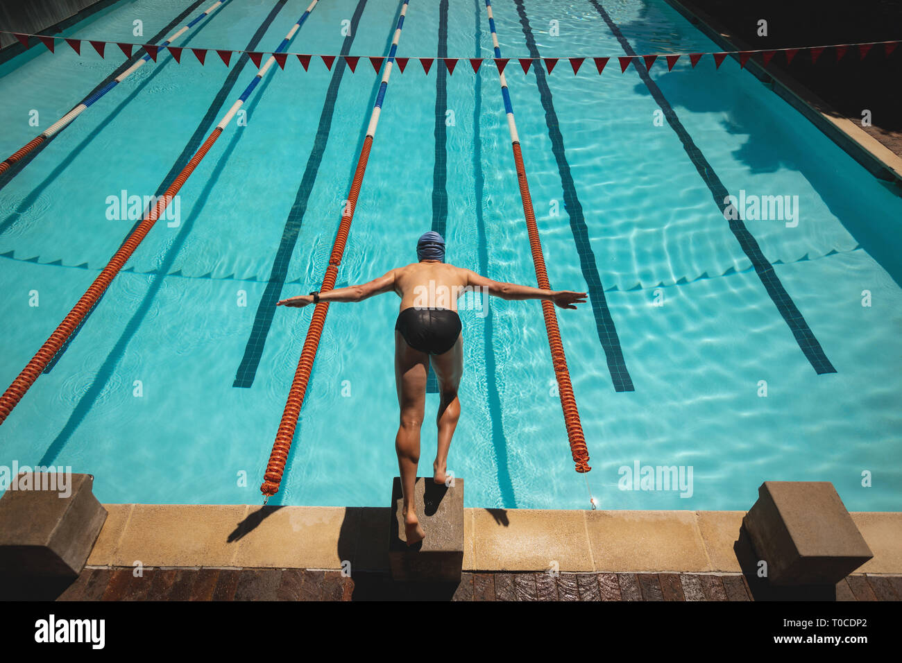 Young male swimmer with arms stretched out jumping into water of a