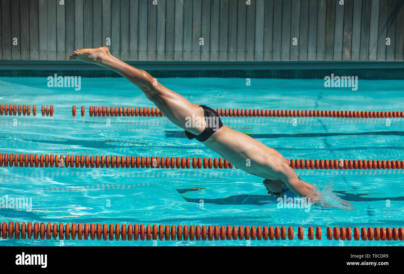 Young male swimmer jumping into water of a swimming pool Stock Photo