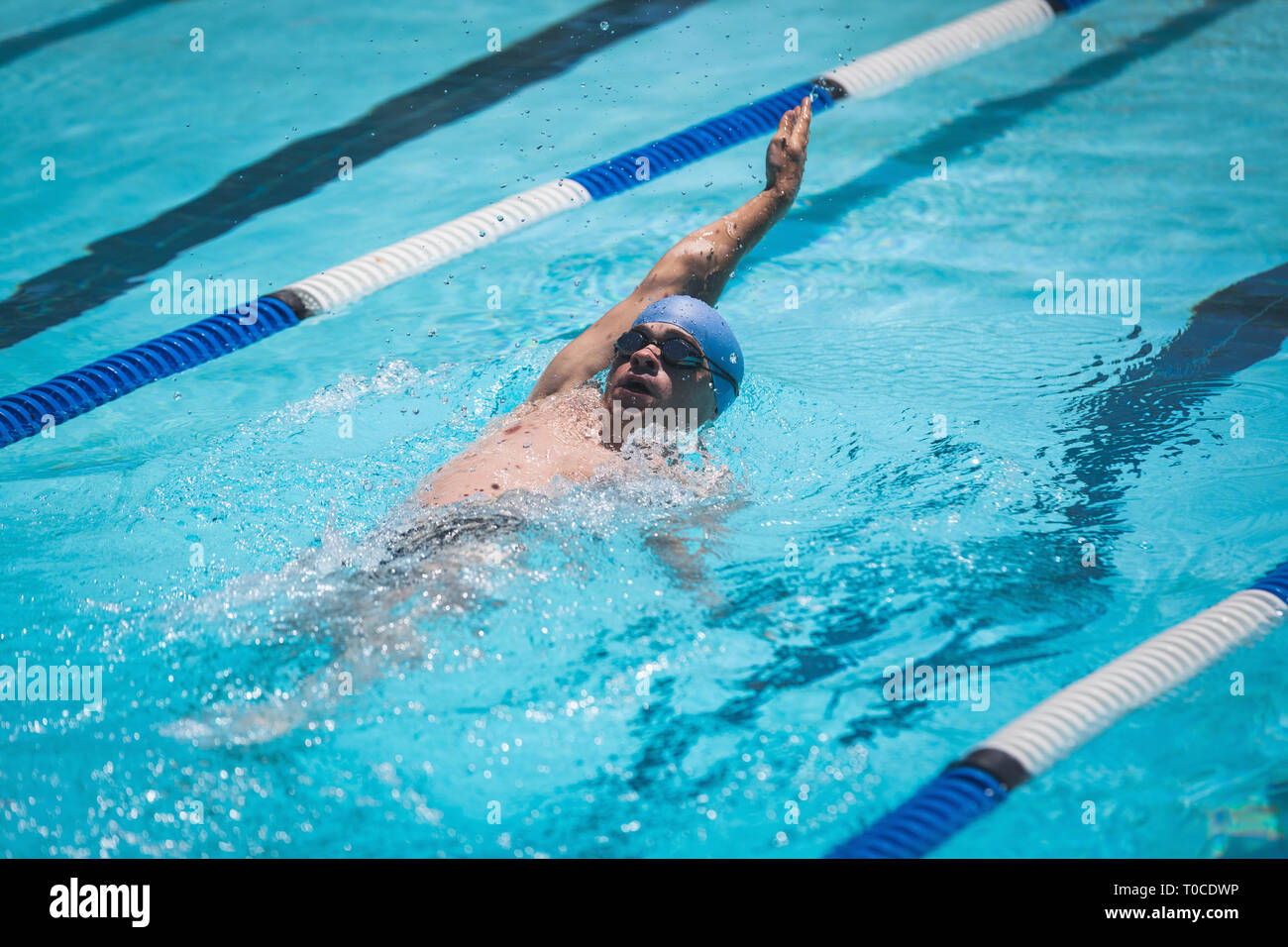 Young Caucasian male swimmer swimming backstroke in swimming pool Stock