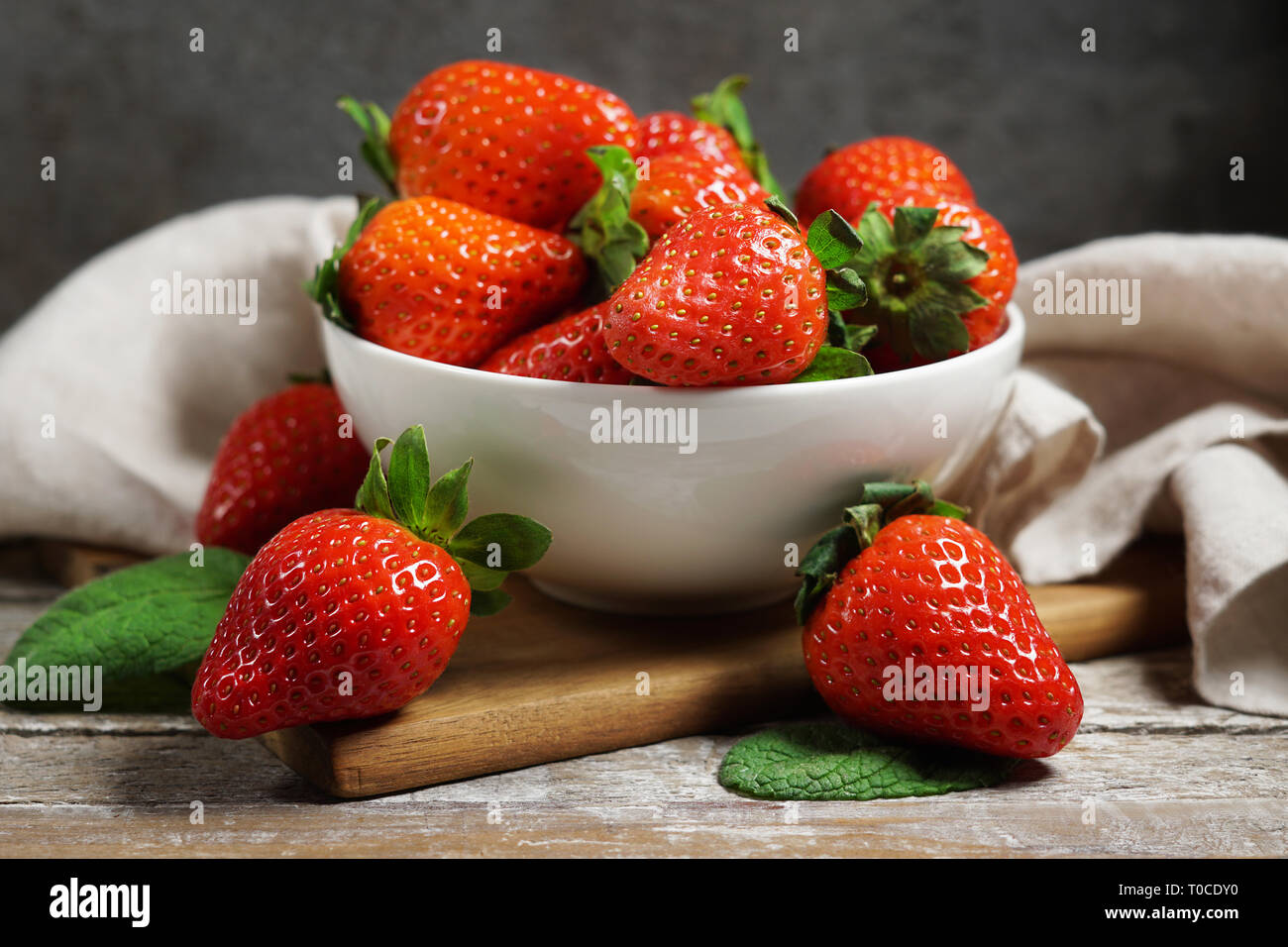 Strawberry concept with a group of ripe red strawberries in a white bowl close up frontal view on a vintage rustic wooden table on background. Stock Photo