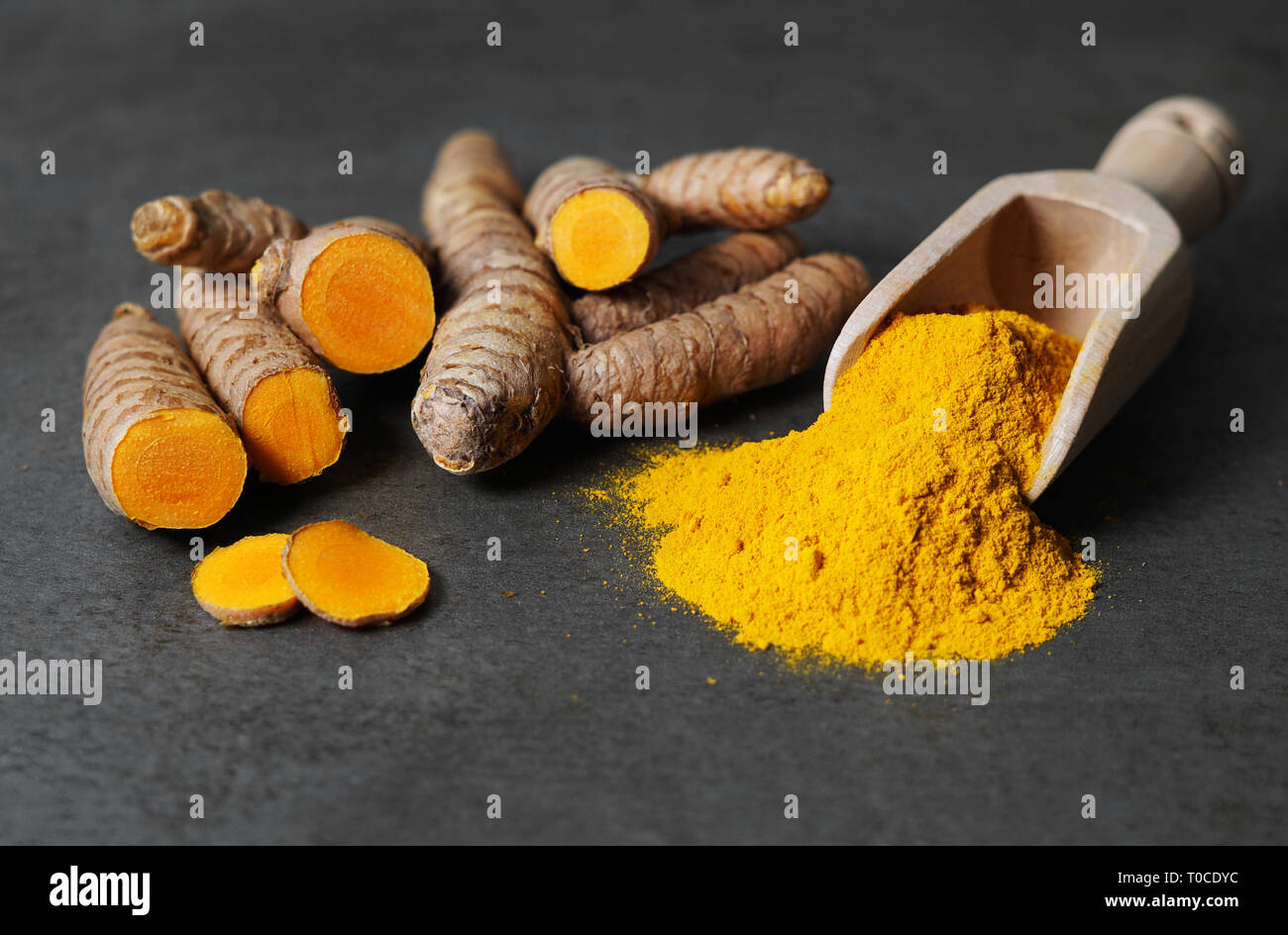 Turmeric powder healthy spice Asian food closeup of turmeric roots sliced and a wooden bailer on a rustic dark grey kitchen board. Stock Photo