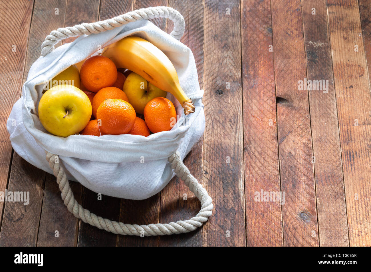 Close-up ecologic white linen bag of fruits on old wooden table. Stock Photo