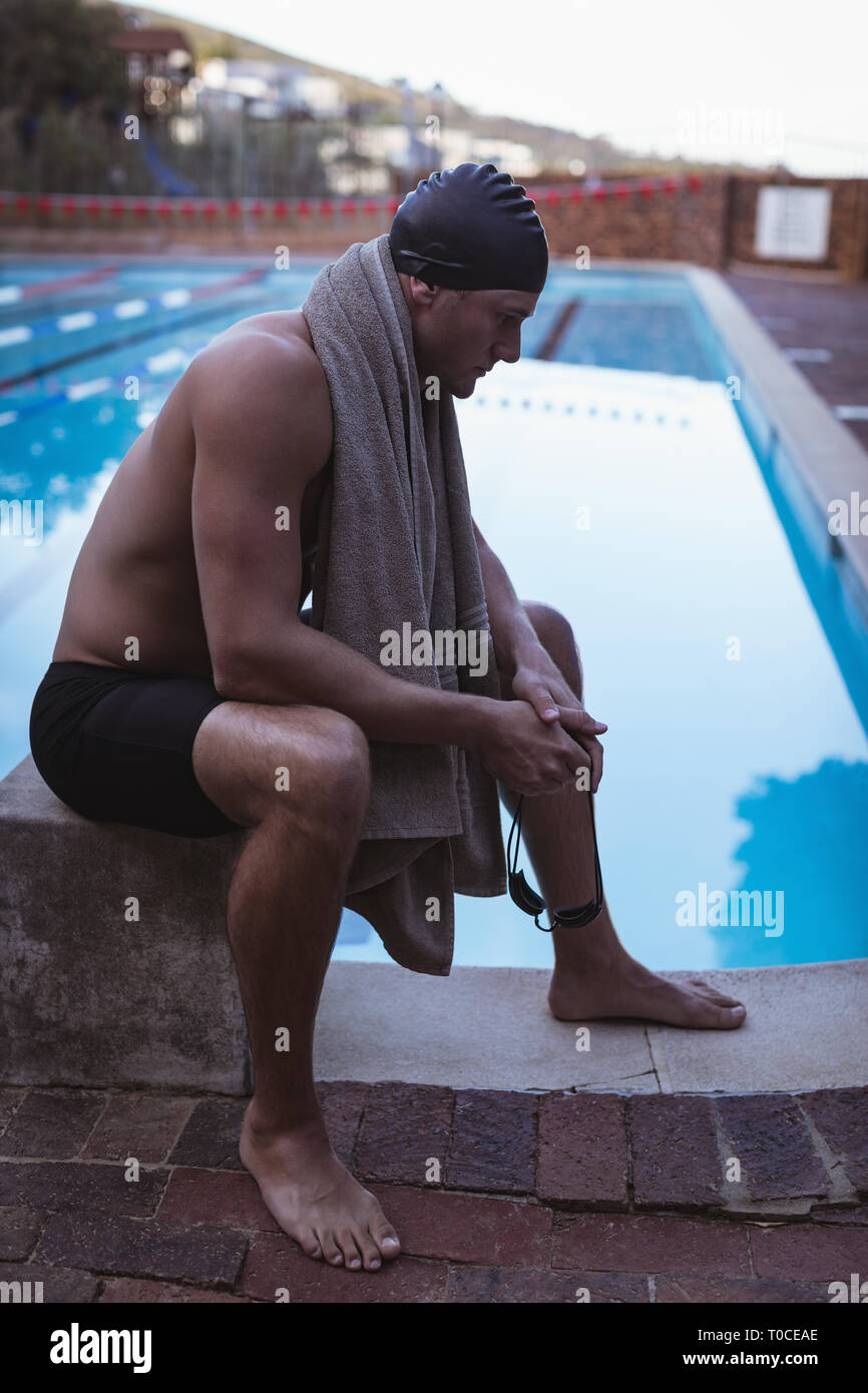 Male swimmer sitting on the starting block near swimming pool Stock Photo