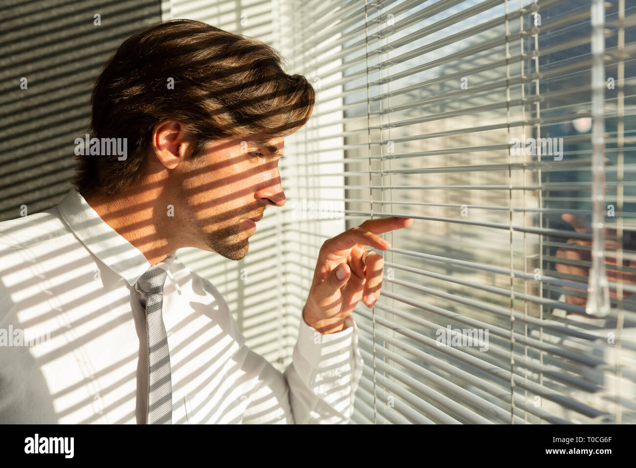 Young Caucasian male executive looking through window blinds in a modern  office Stock Photo - Alamy