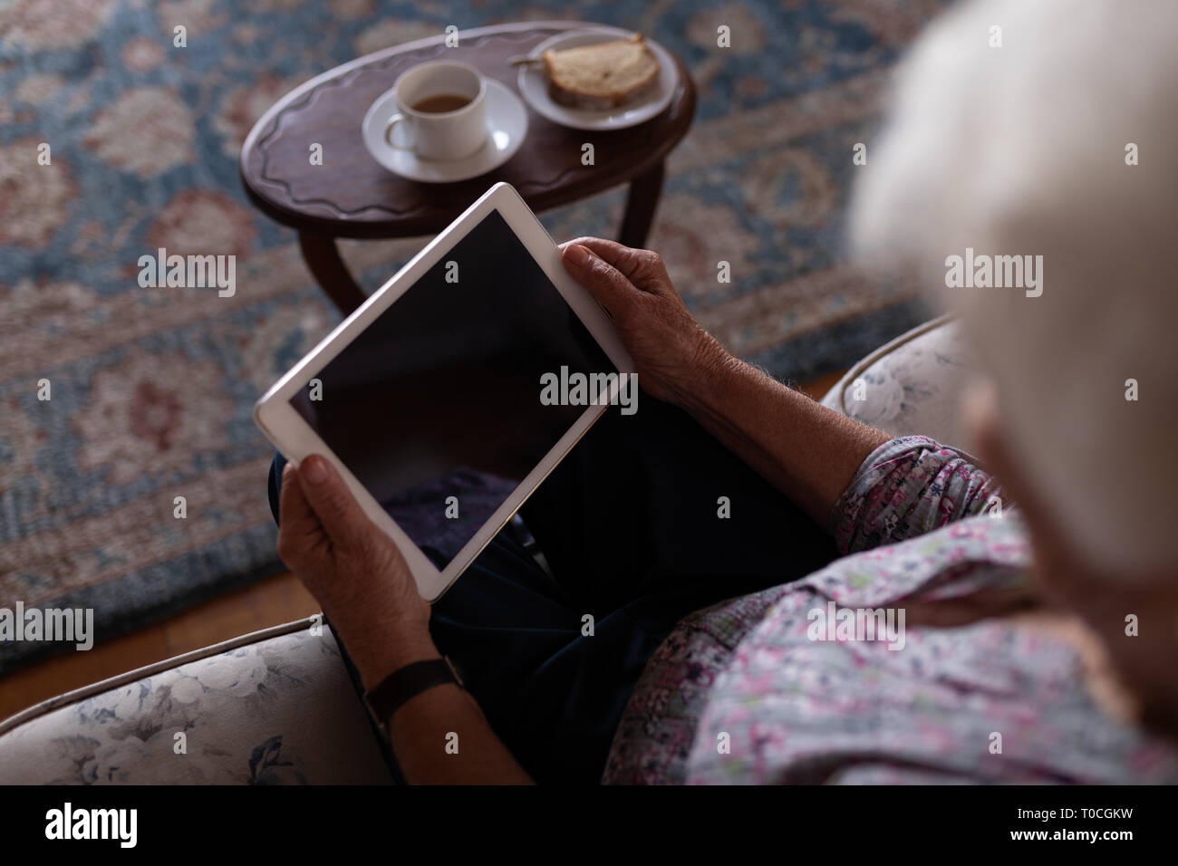 Active senior woman using digital tablet while sitting on the sofa at ...