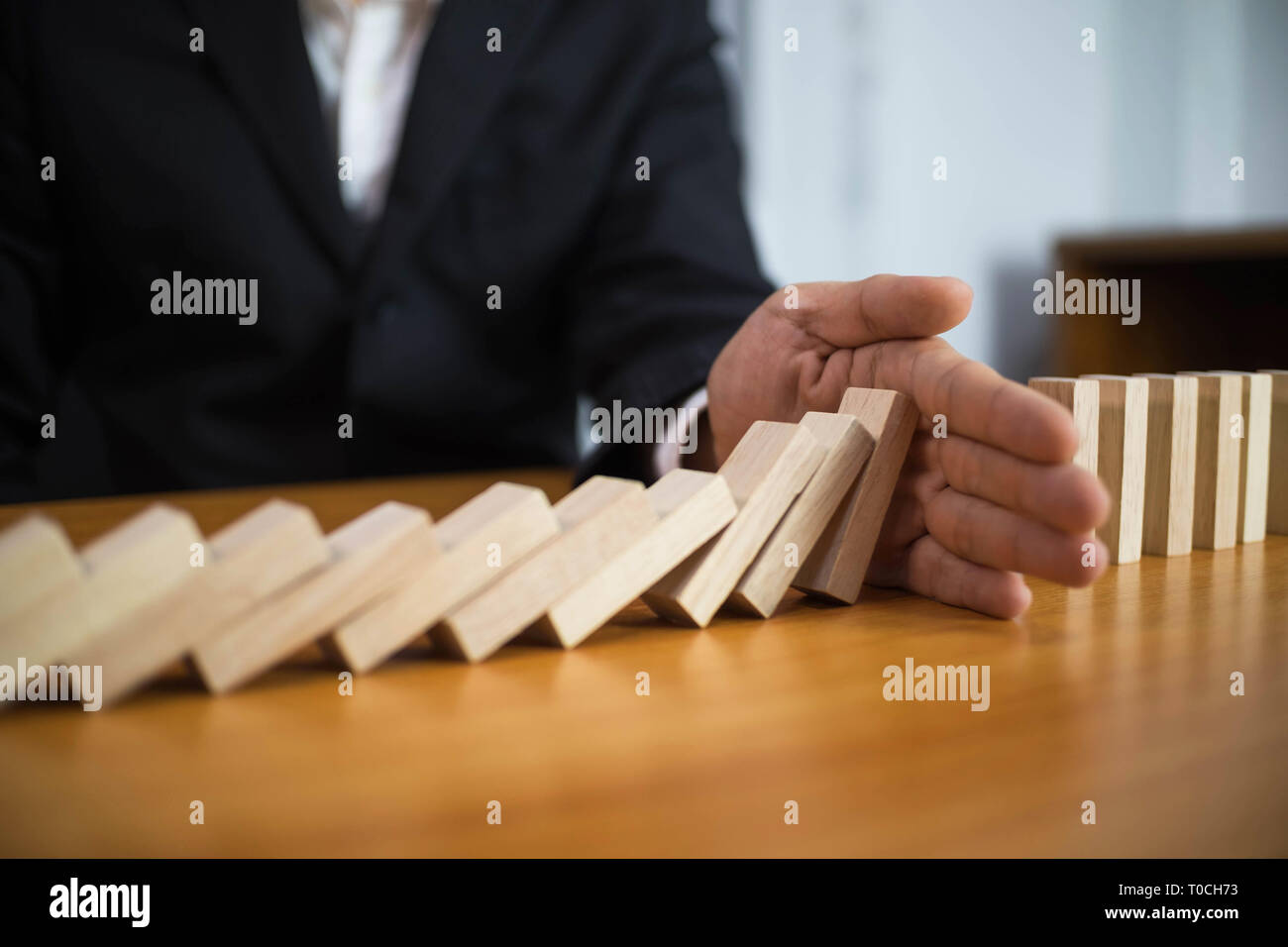 Businessman hand stops domino continuous overturned meaning that