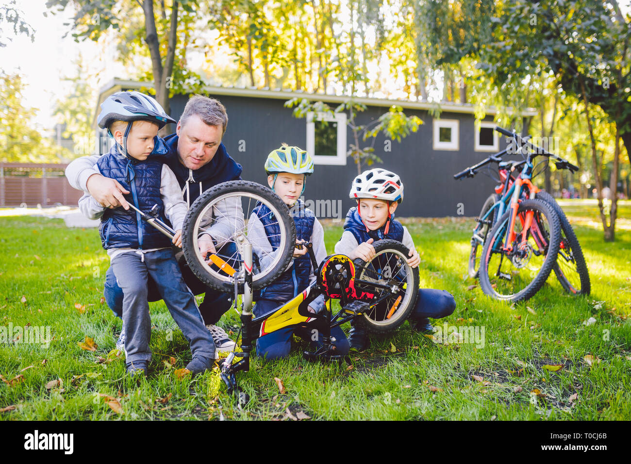 Father's day A big friendly family father and three sons joint active rest outside. Dad teaches sons to repair cycling. The child uses the pump tool Stock Photo