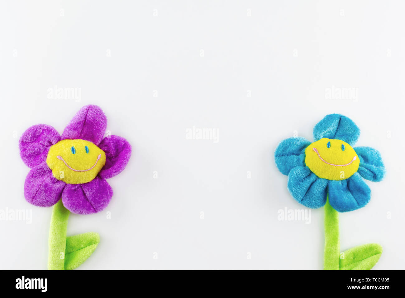 Two toy plush smiling flowers on a white background, one on each side.  Copy space in the middle and above. Stock Photo