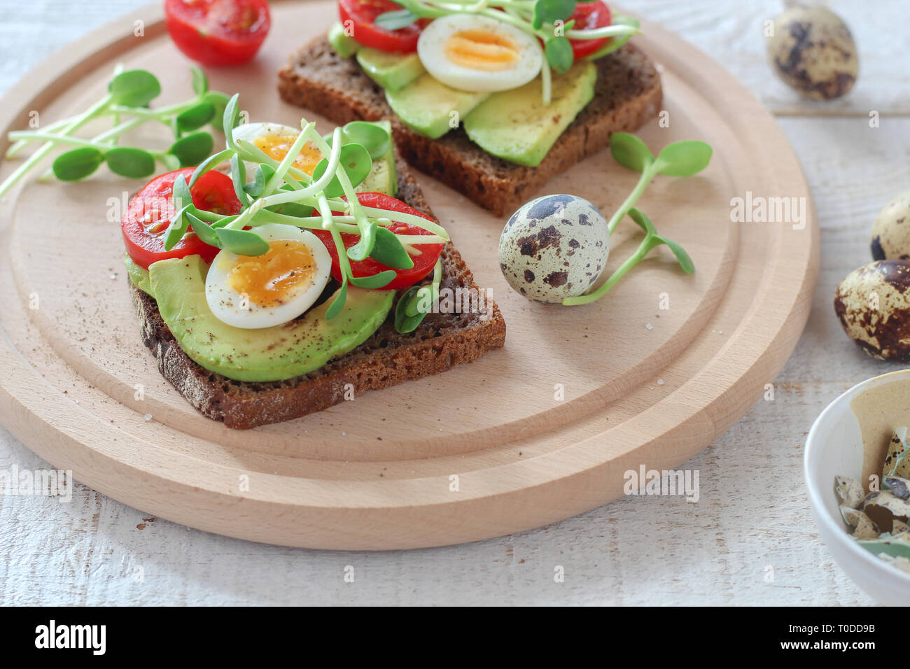 Healthy sandwiches with avocado, tomato, quail eggs and sunflowers micro greens (sprouts) on a white wooden background Stock Photo