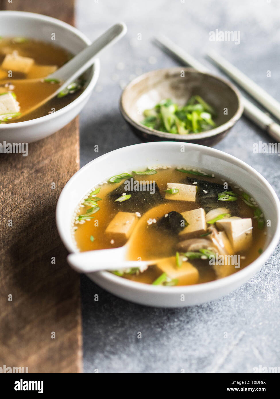 Japanese miso soup with oyster mushrooms in a bowls with a spoon and white chopsticks on a grey and wood backgrounds. Stock Photo