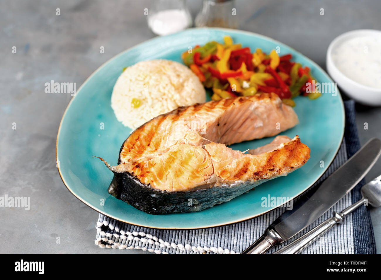 Grilled salmon steak with steamed paprika and rice on grey background