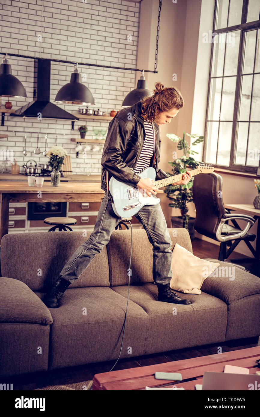 Rock player standing on sofa while playing hard rock song Stock Photo