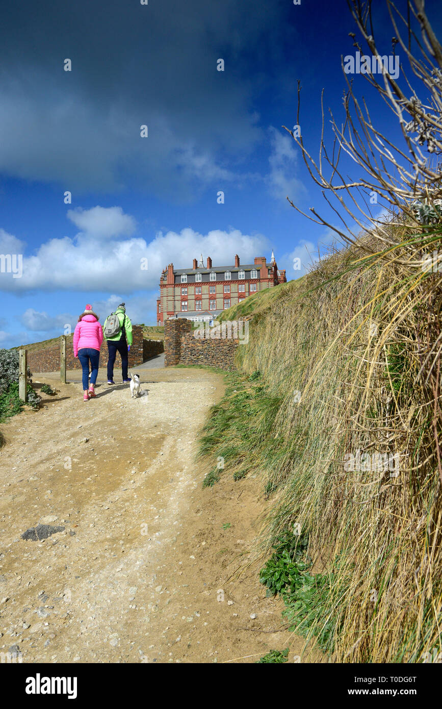 Dog walkers wearing brightly coloured jackets walking along the coastal path near the Headland Hotel in Newquay in Cornwall. Stock Photo