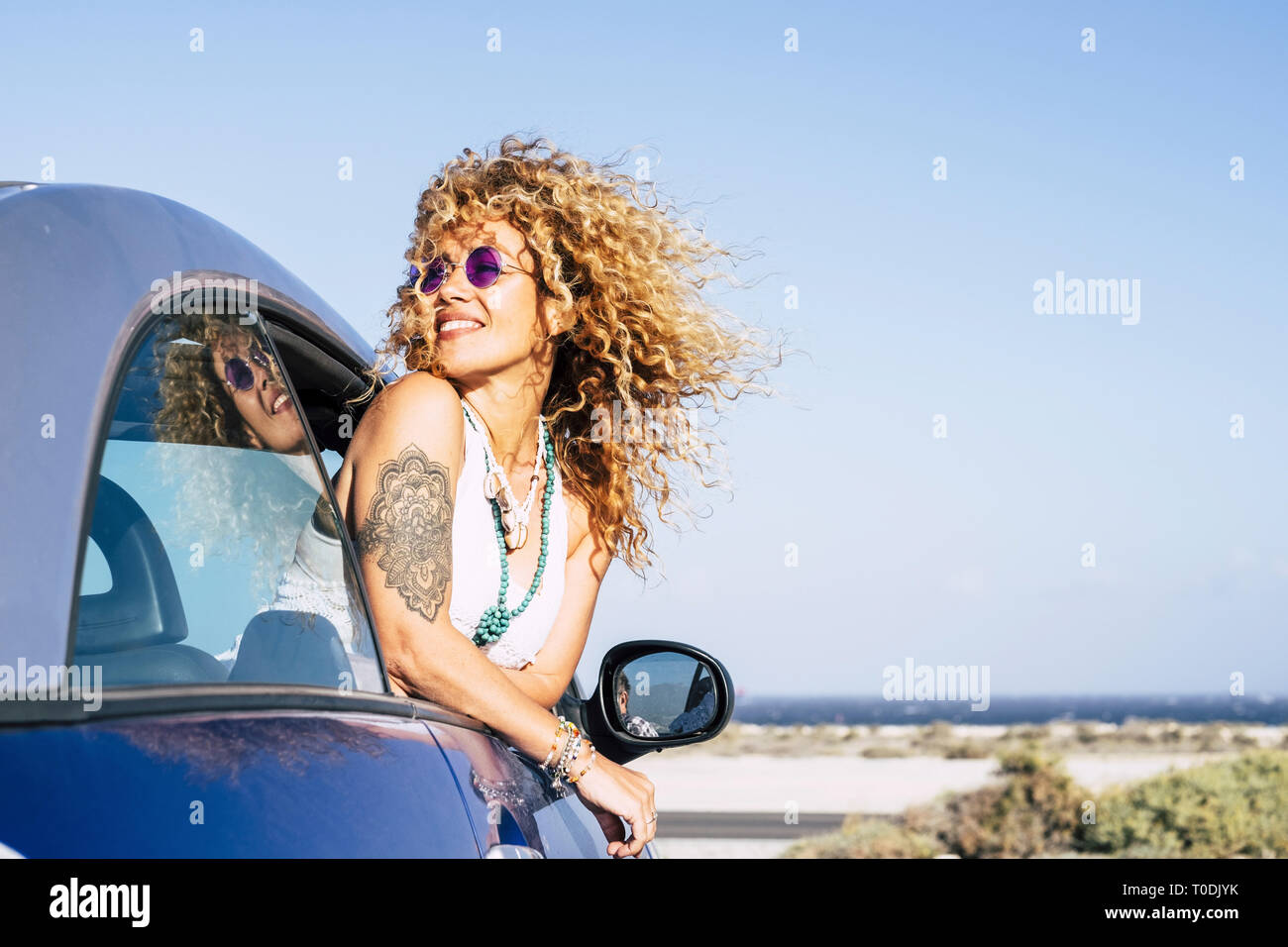 Beautiful cheerful happy caucasian woman outside the car with wind in curly long blonde hair - attractive people enjoying the freedom in outdoor coast Stock Photo