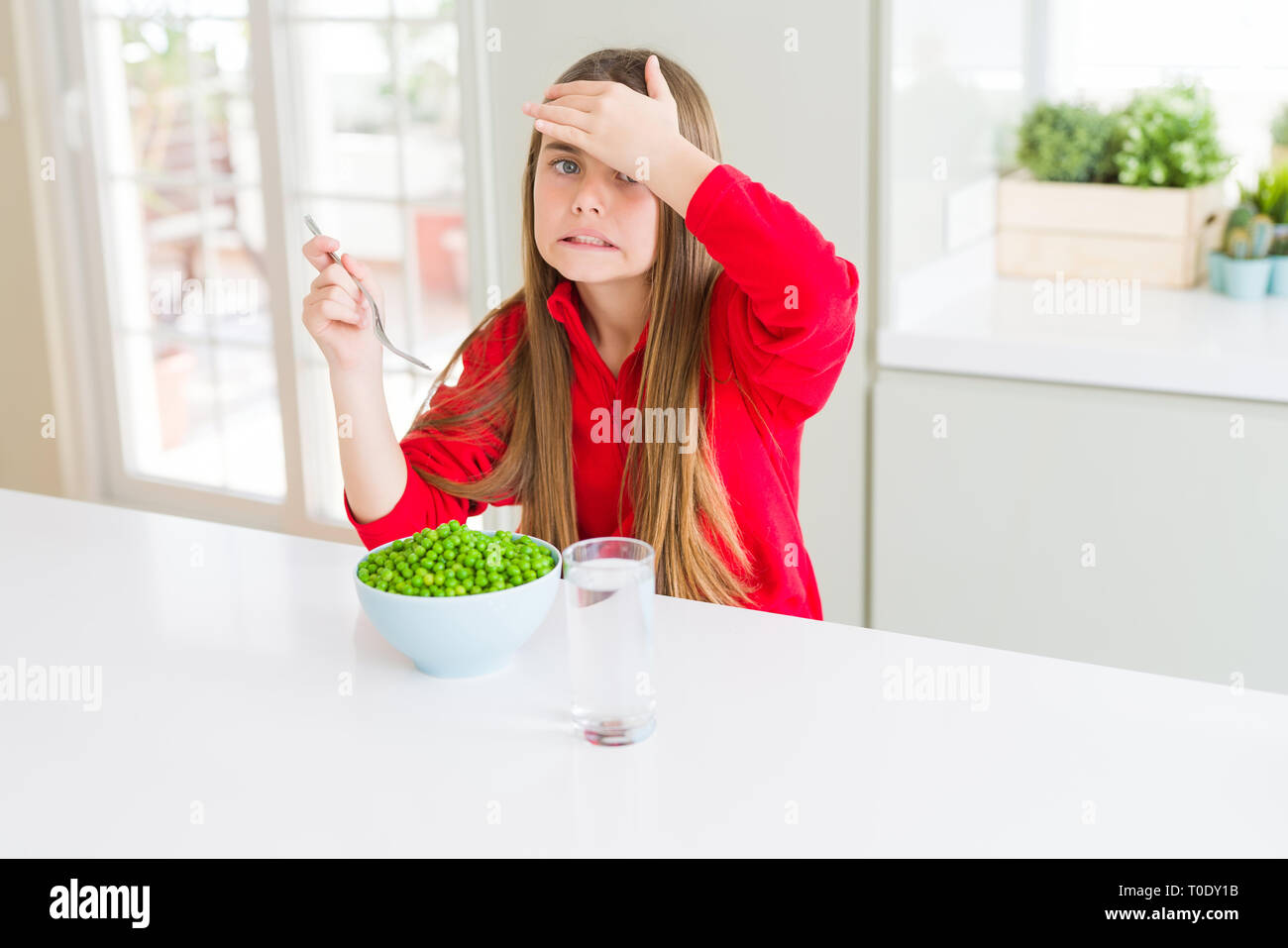 Beautiful young girl eating healthy green peas stressed with hand on