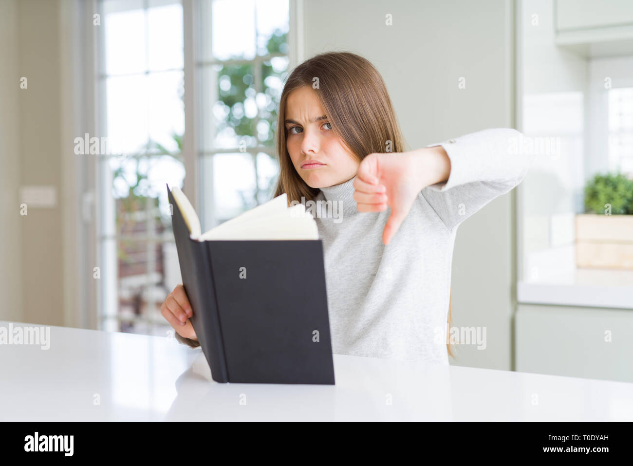 Beautiful young girl reading a book at home with angry face, negative ...