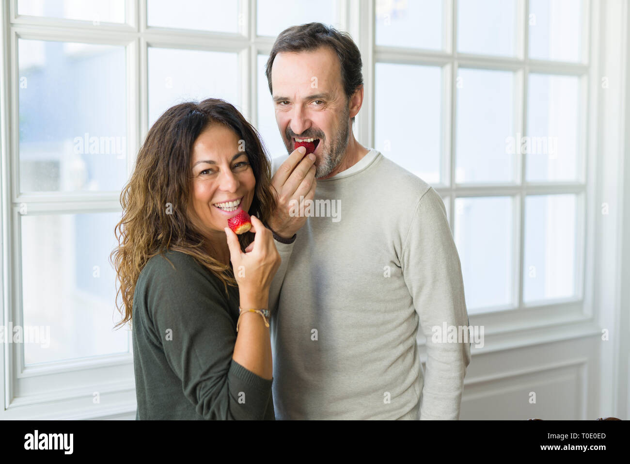 Middle age senior couple eating a fresh strawberry at home Stock Photo